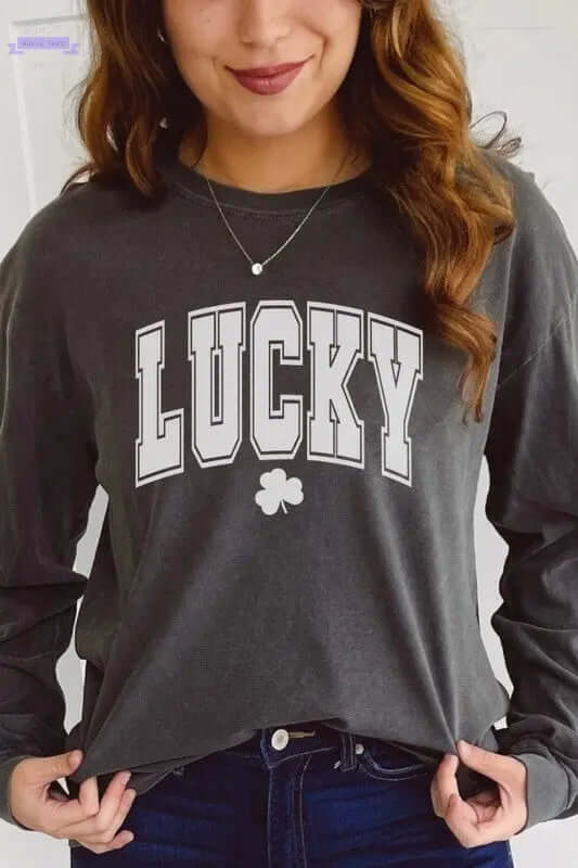 Woman wearing a gray long sleeve St. Patrick's Day shirt with 'LUCKY' graphic and shamrock emblem.