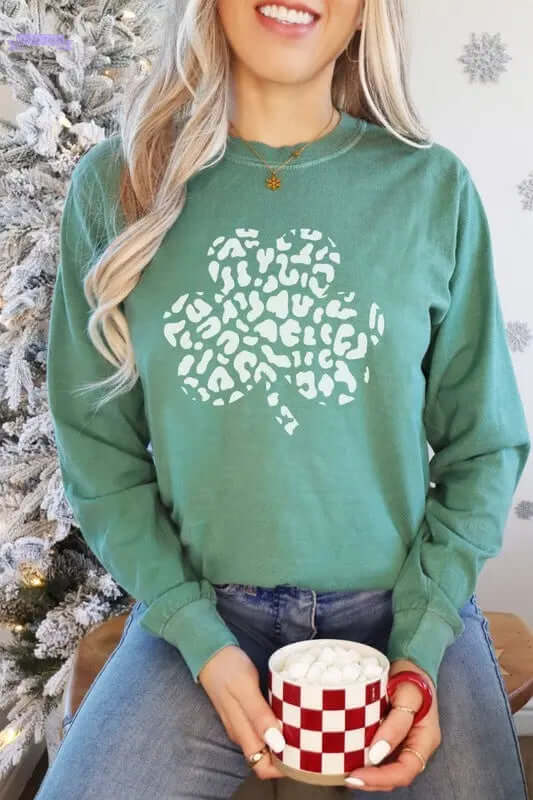 Woman wearing a green long sleeve shirt with a leopard print shamrock design, holding a mug with marshmallows.