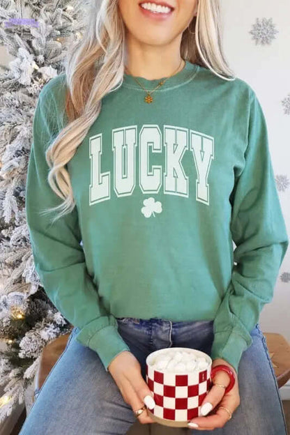 Woman in a green long sleeve shirt with "LUCKY" graphic, holding a checkered mug, celebrating St. Patrick's Day.