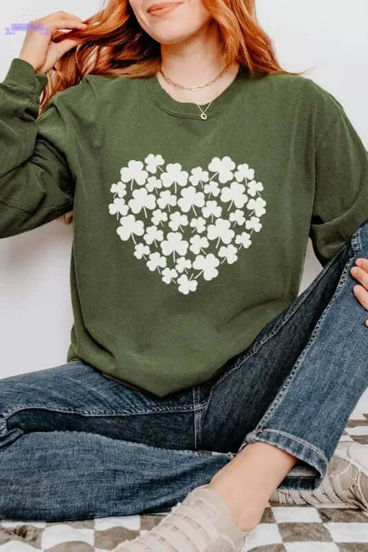 Woman wearing a green long sleeve shirt with a white shamrock heart design for St Patrick's Day celebration.