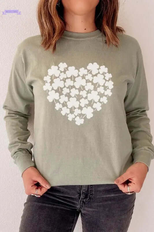 Woman wearing a light green long sleeve tee featuring a shamrock heart design for St. Patrick's Day celebration.